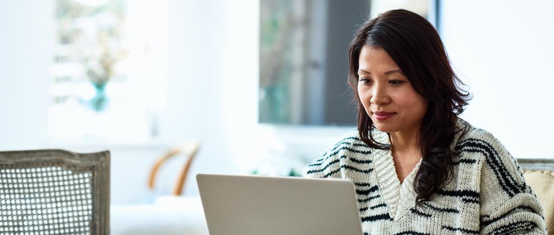 Mid adult woman in her 30s sitting at table and looking at computer, remote working, freelancer, small business